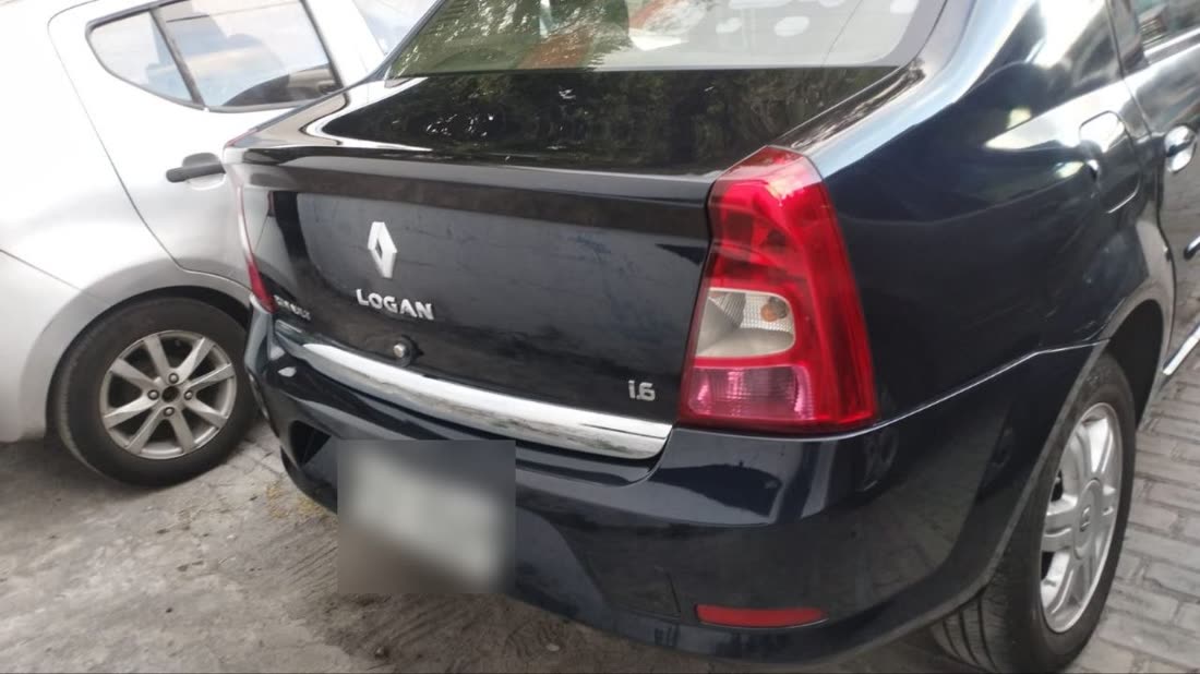 Parte trasera de un Renault Logan negro con el guardachoque hundido, tal como llego al taller